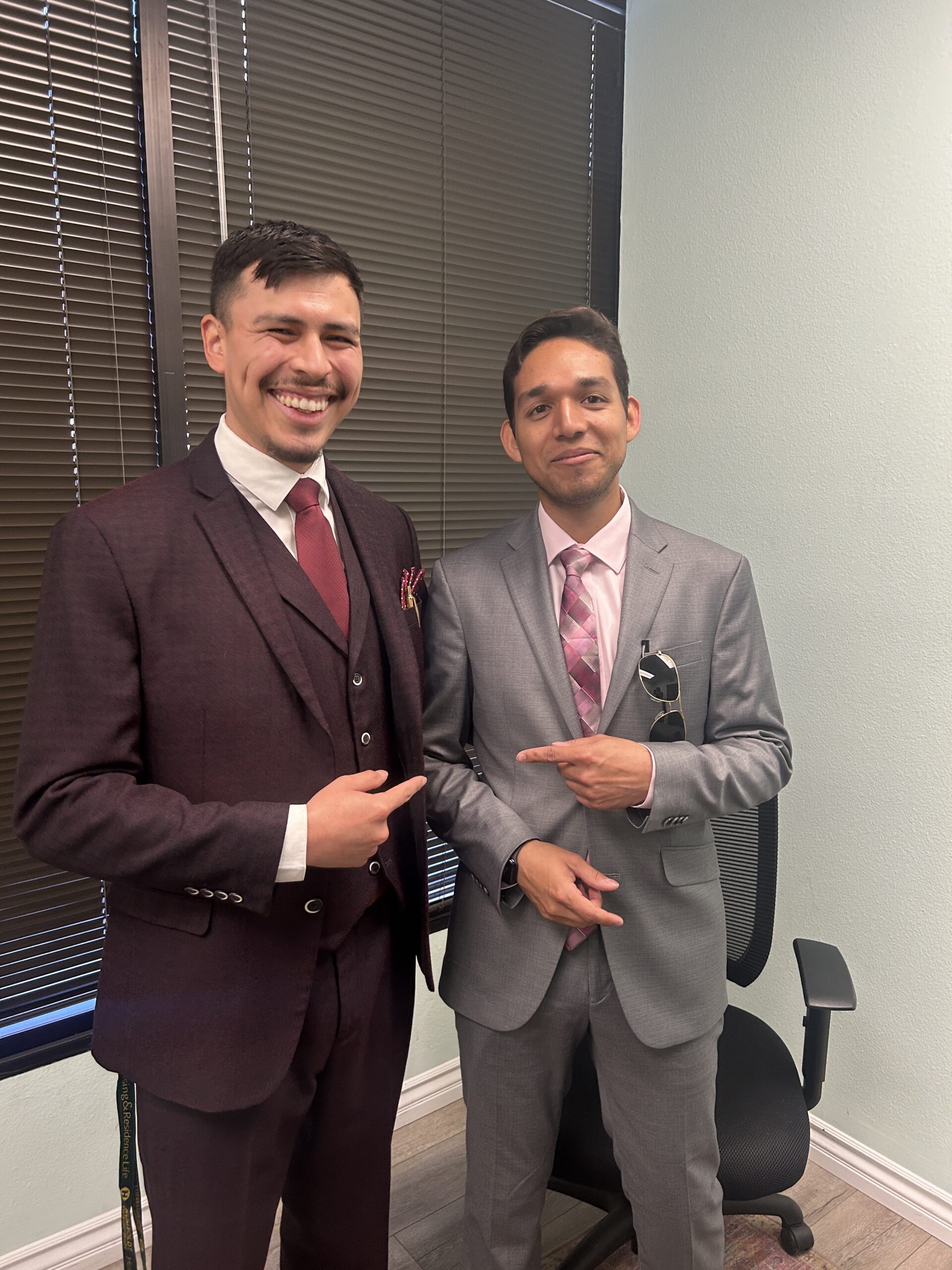 Two smiling businessmen in tailored suits posing together in a modern executive office.