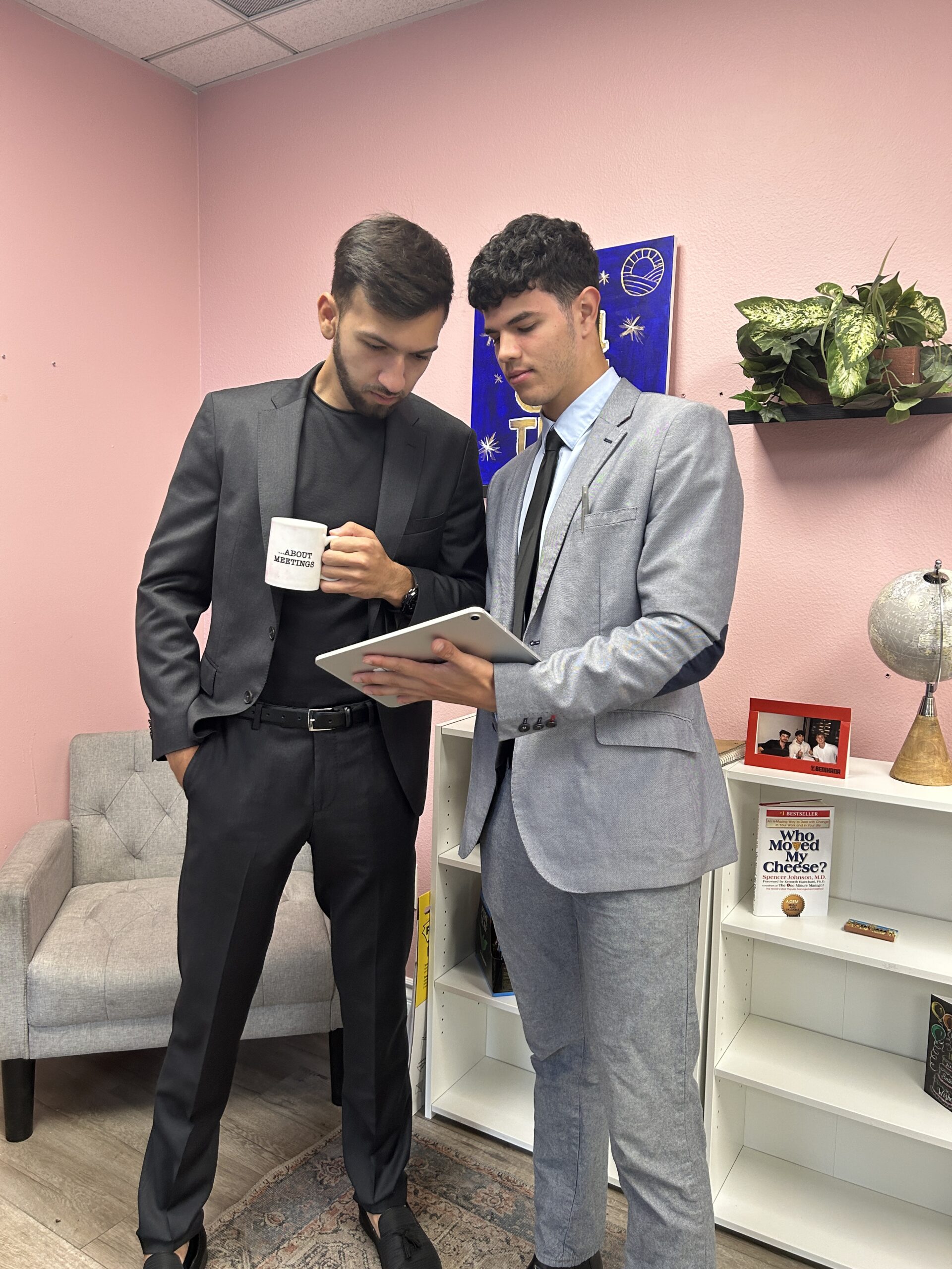 Two young businessmen in professional suits discussing analytics on a digital tablet in a modern office.